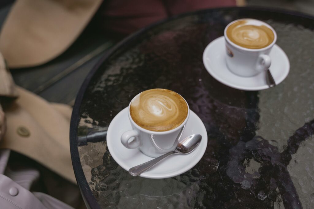 Two frothy cappuccinos with latte art on a glass table in a cozy café setting.